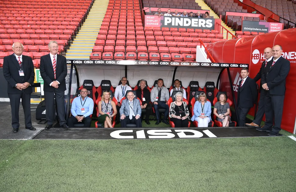 MEPS Staff in the dugout at Bramall Lane, surrounded by Sheffield United legends