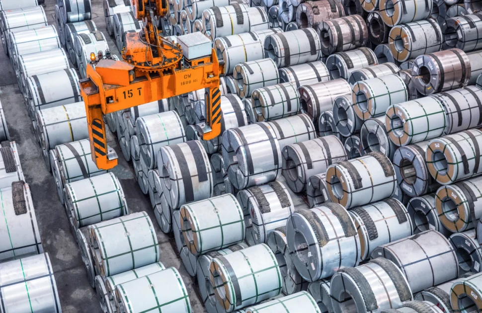 A crane hovers over steel coil stocks